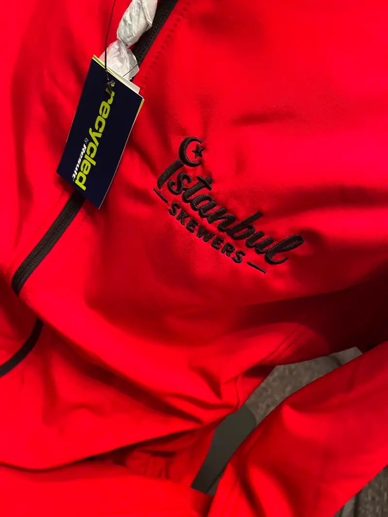 Close-up of the Istanbul Skewers logo embroidered in black thread on red softshell fabric